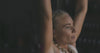 Woman performing a pull-up exercise on a bar in a dimly lit gym.
