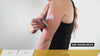 Person placing a round adhesive patch on the upper arm while wearing a black sleeveless top.